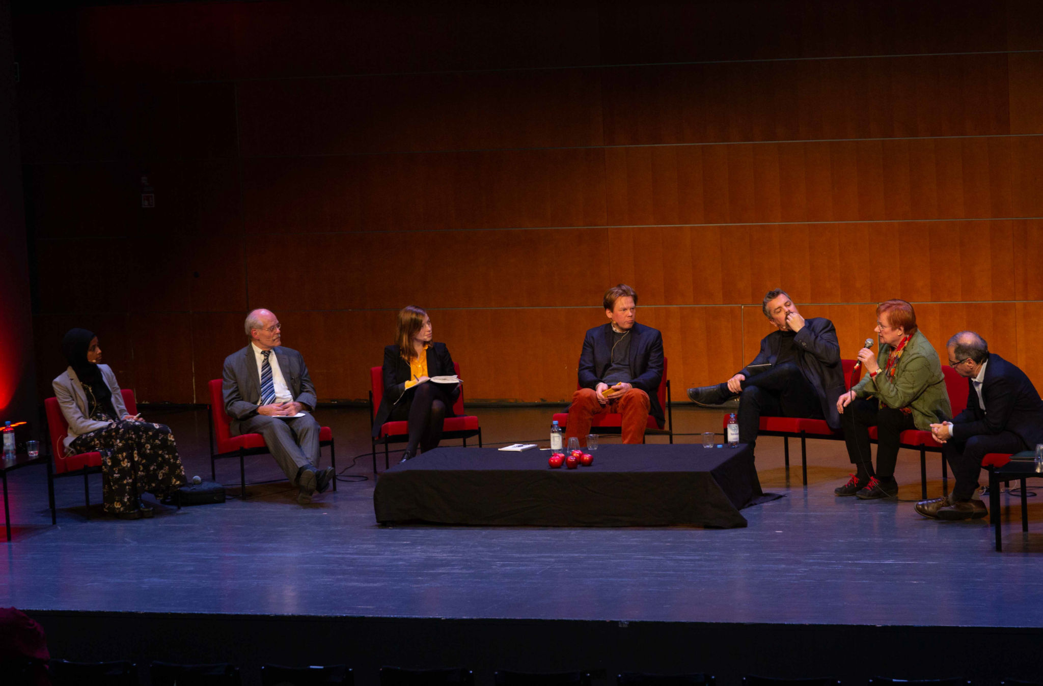 Scen med panelen vid Imagine! Från vänster sitter Maryan Abdulkarim, Stefan Ingves, Li Andersson, Dan Lolax, Alf Rehn, Tarja Halonen och Göran Rosenberg med ett bord i mitten.