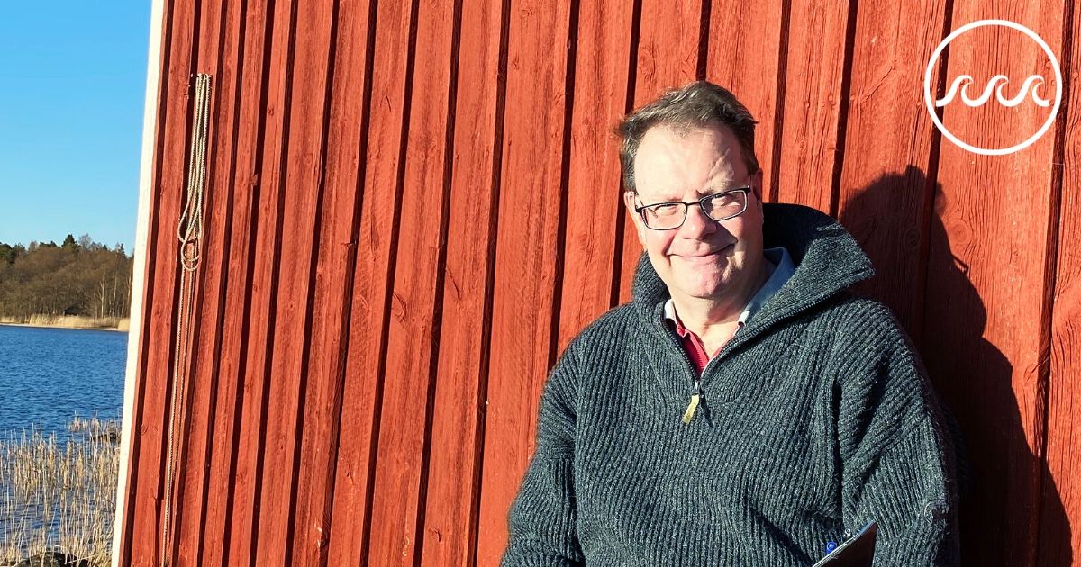 Marko Joas sitter framför en röd fiskestuga vid havet