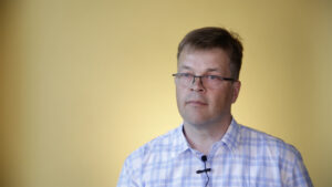 Ronald Österbacka i blåvitrutig skjorta, framför gul bakgrund.