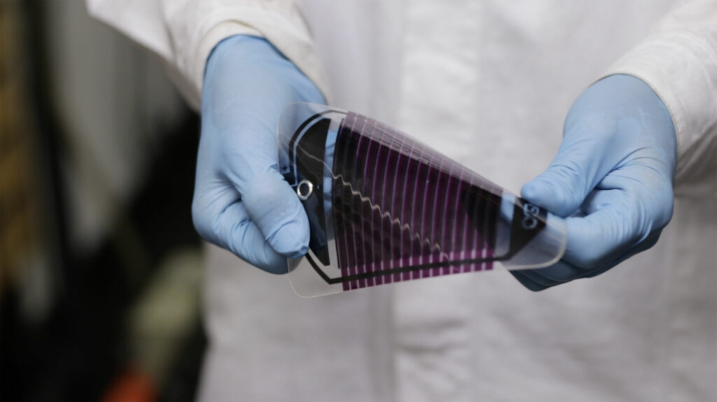 Person i labbrock och med blåa labbhandskar, böjer på solcell i plast.