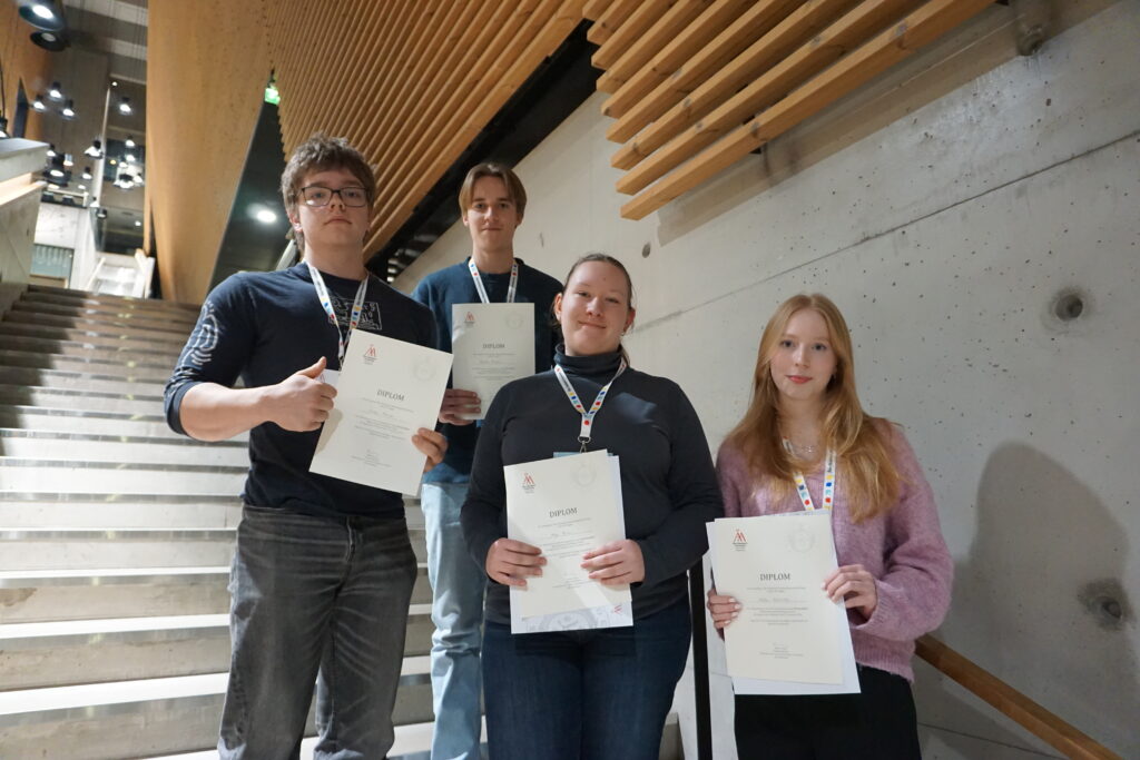 Fyra gymnasiestuderande står i trappan i Aurum och ler efftersom de vunnit första plats i diplomingenjörstvlingen under DI-dagen 2026.